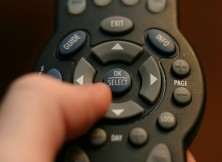 A hand holds a cable TV remote control.