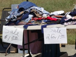Clothing on a table at a garage sale with sign '2 for $1.00'.